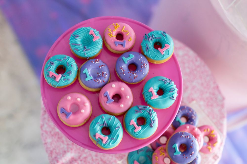 Colorful mini donuts in pink, blue and purple arranged on a pink serving plate.