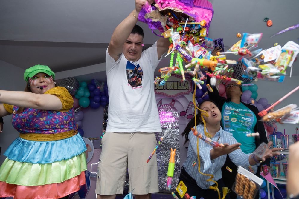 People at a party reaching for colorful piñatas hanging from the ceiling during a festive celebration.