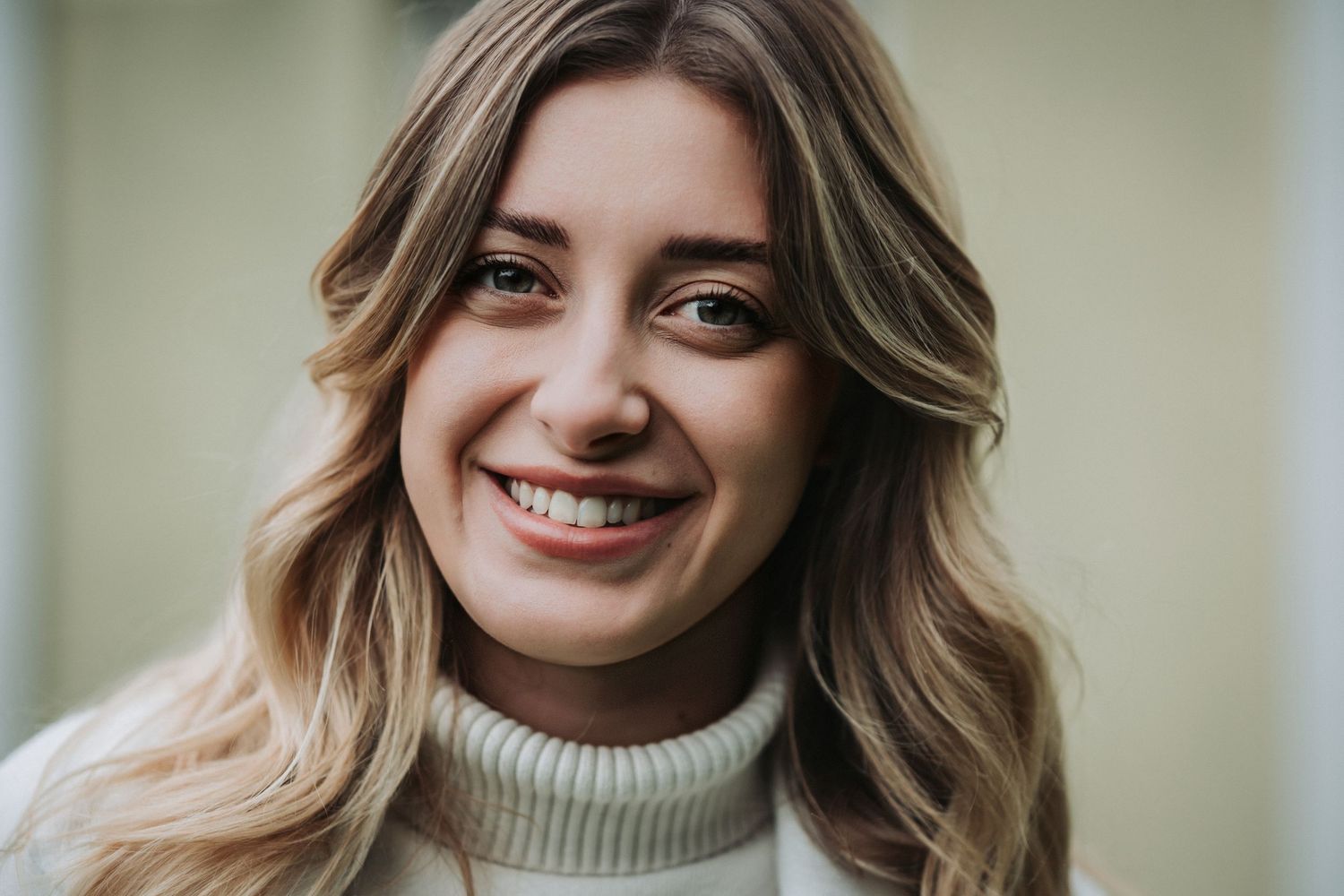 Close up portrait of woman in cream turtleneck sweater with wavy blonde hair.