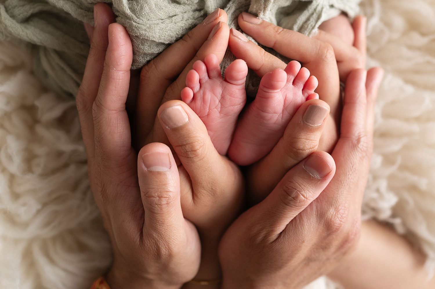Tiny newborn feet cradled gently in adult hands on soft textured background.
