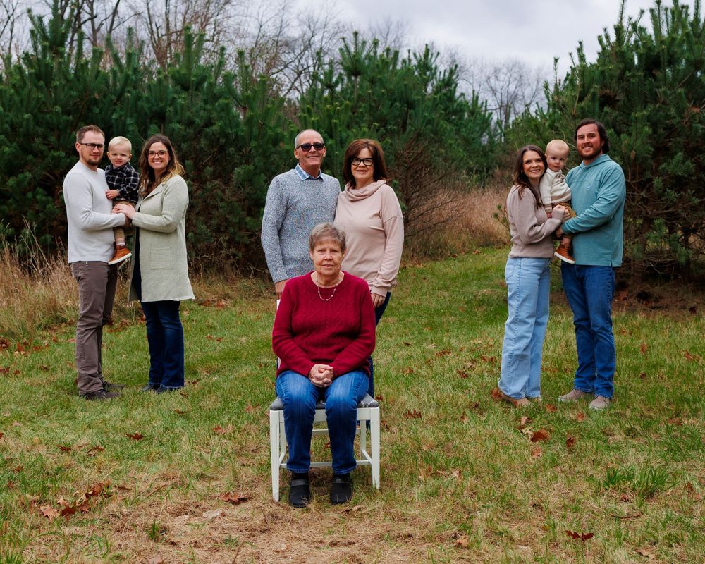 A family group poses together outdoors in front of evergreen trees during an autumn day.