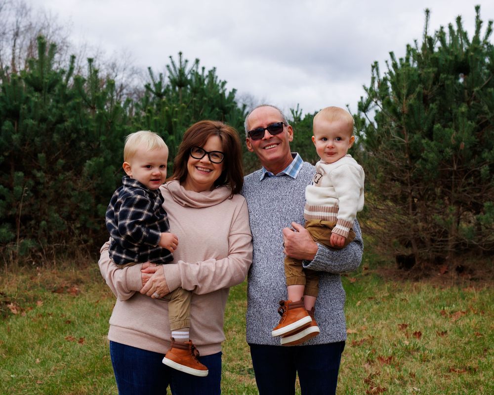 Group poses for outdoor family photo in front of evergreen trees on cloudy day.