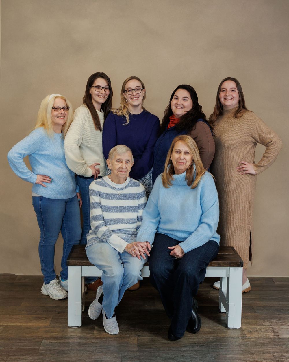 Group photo of seven people wearing casual sweaters and jeans seated and standing together against a neutral wall.