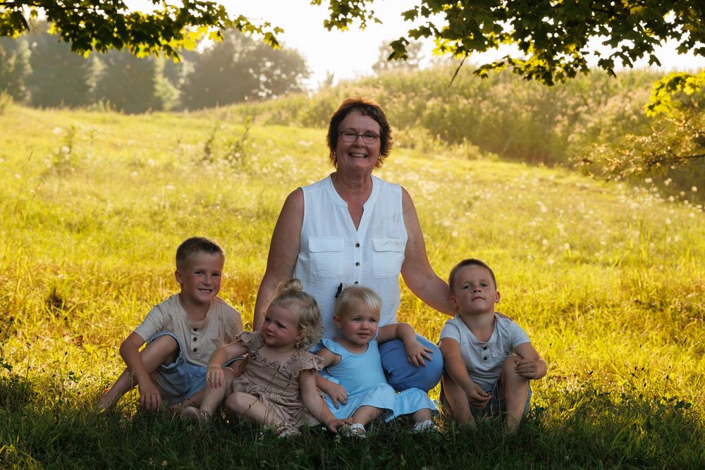 A group sits together on a grassy hillside during golden hour in a pastoral summer setting.