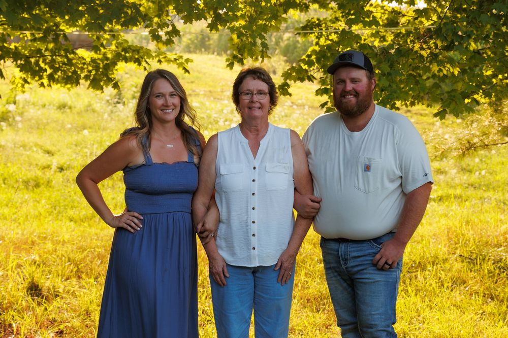 A group poses together in a sunny outdoor setting with golden light filtering through trees.