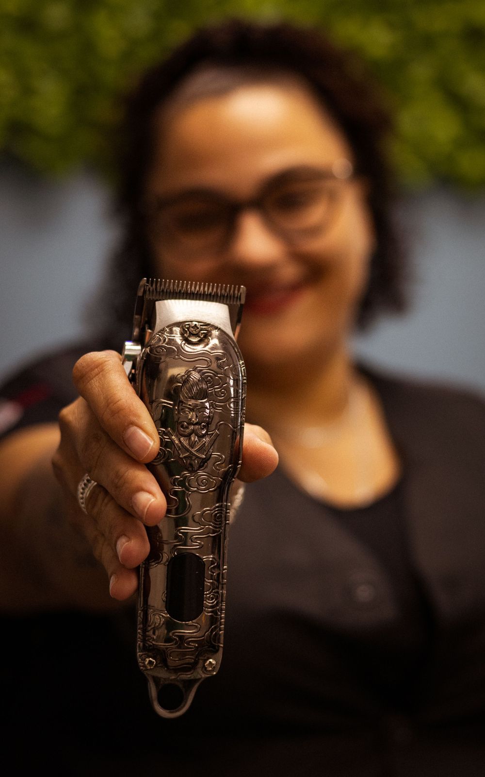 Vintage-style hair clipper being displayed against green foliage background.
