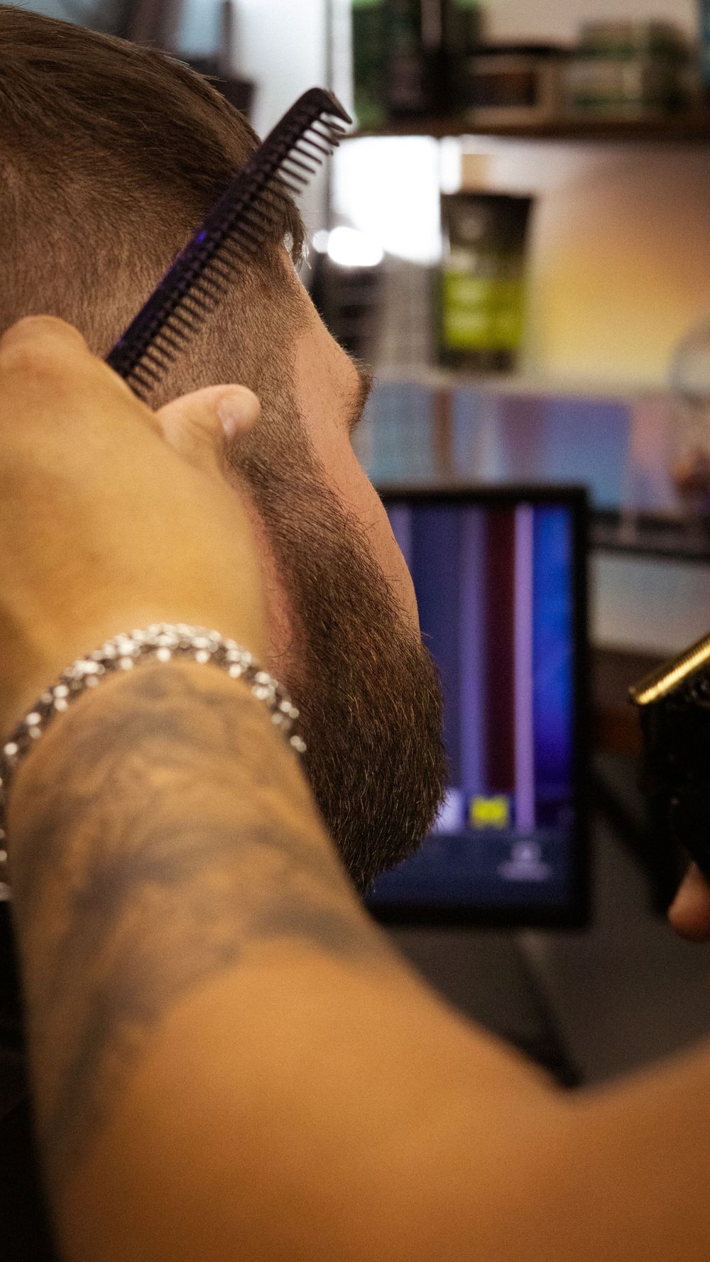 Tattooed barber's hand holding a comb while performing a precise haircut.