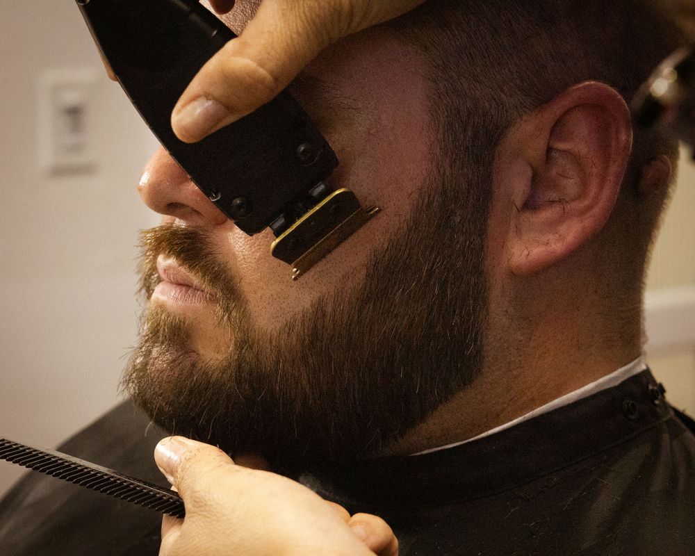 Close-up of beard trimming with professional clippers showing precise grooming technique.