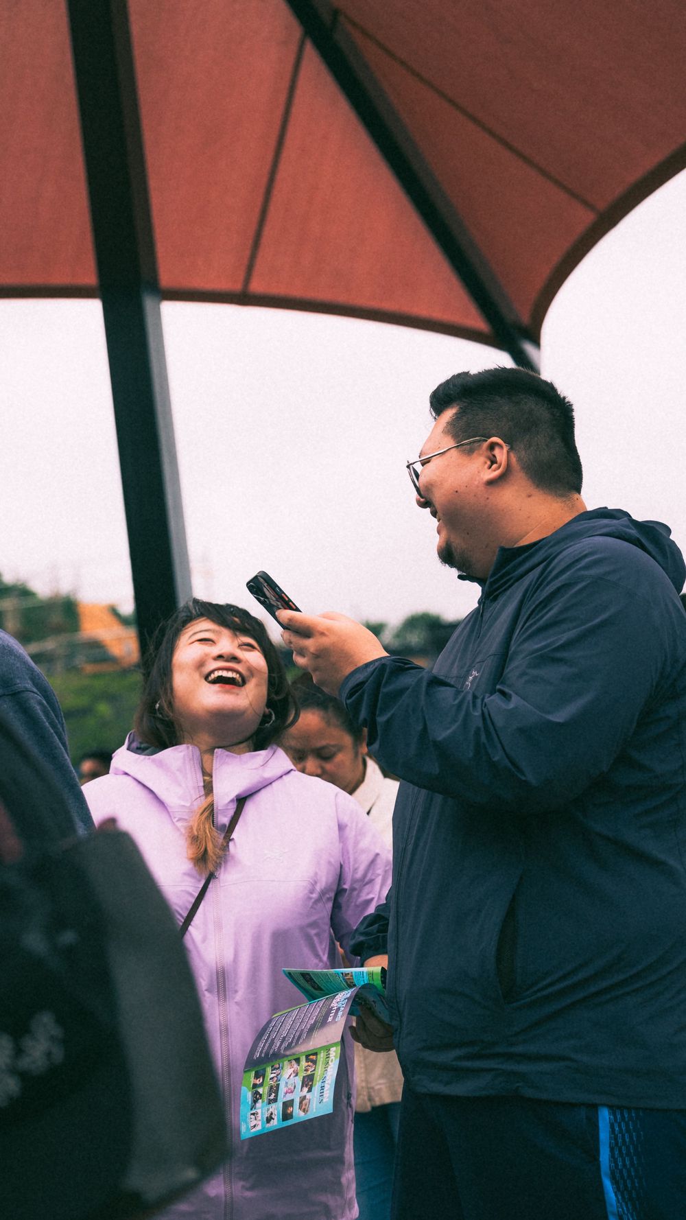 People sharing a moment under a large red umbrella or canopy outdoors.