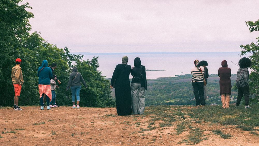 People gather along a scenic mountain overlook with views of a distant landscape.
