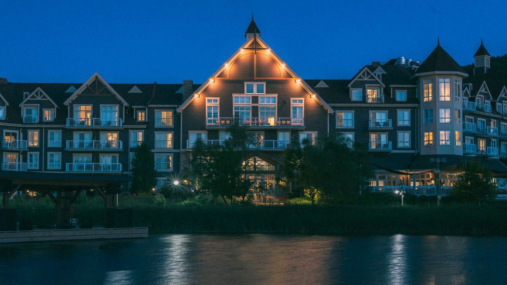 Row of waterfront townhouses illuminated at dusk with reflections on calm water.