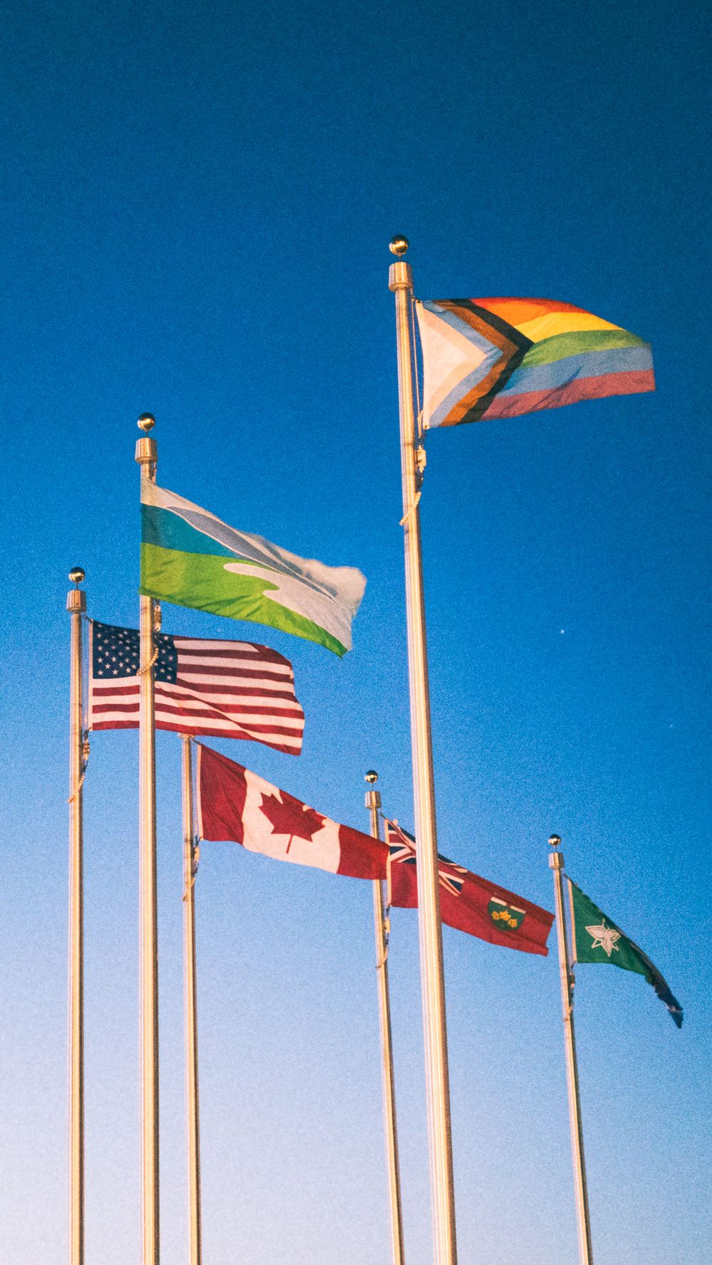 Various international flags waving against a bright blue sky.