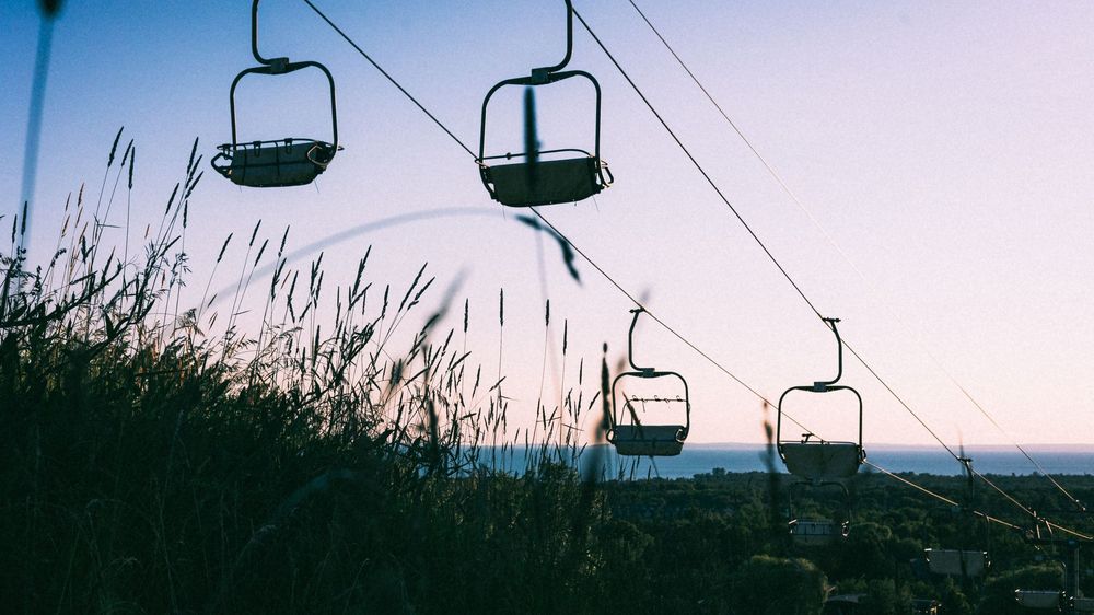 Silhouettes of empty ski lifts against a pastel sunset sky.