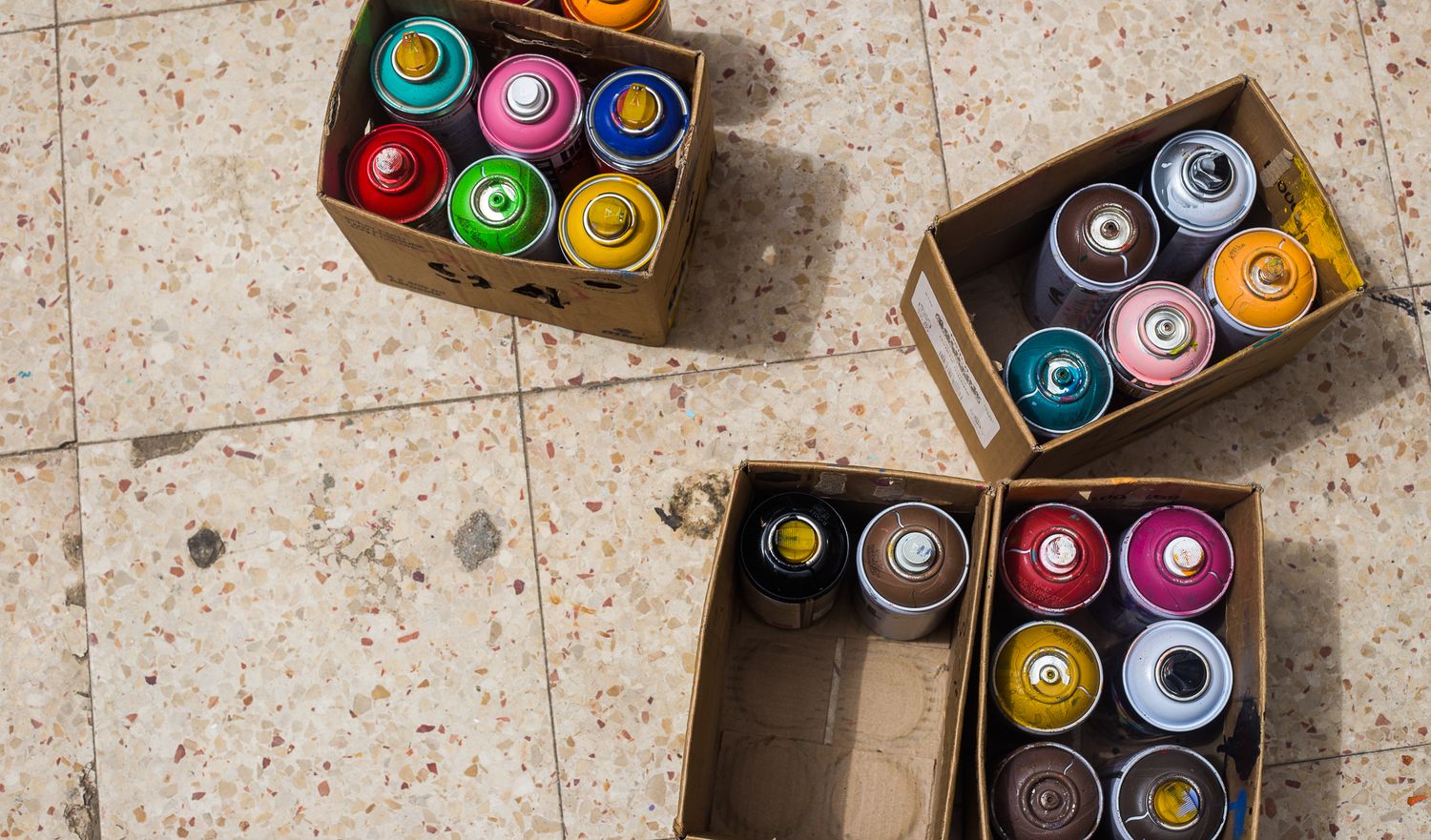 Collection of colorful spray paint cans arranged in cardboard boxes.