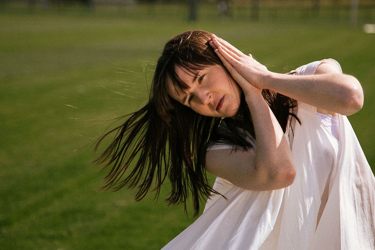 Person in white dress dancing outdoors with flowing hair motion in sunlight.