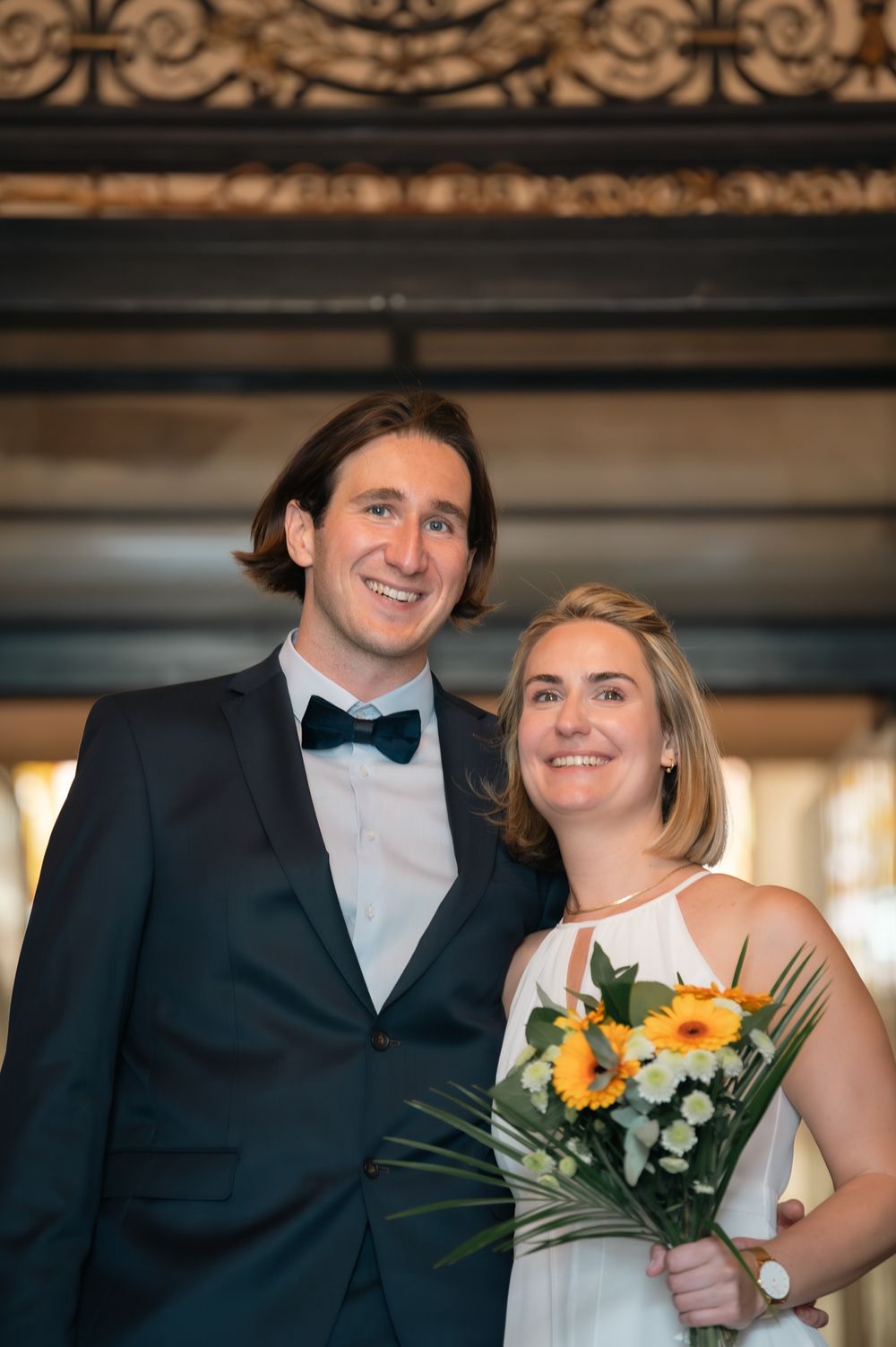 Happy wedding couple posing together with sunflower bouquet in formal attire.