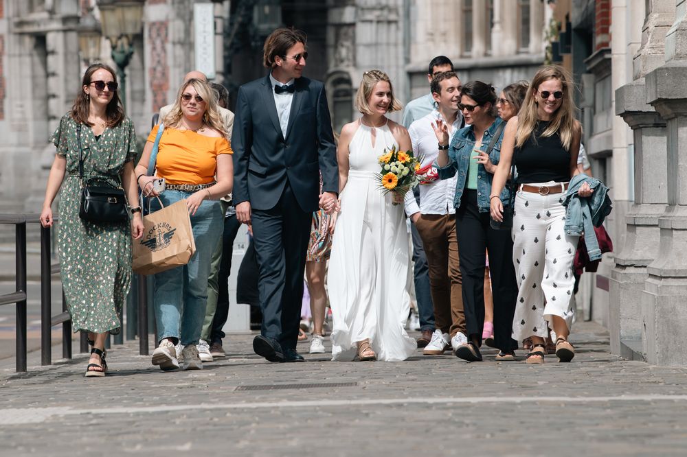 Wedding party and guests gathering outside historic building on sunny day.