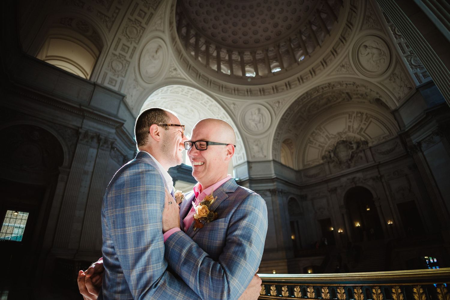 Two people embrace under an ornate domed ceiling in a historic building during a wedding ceremony.