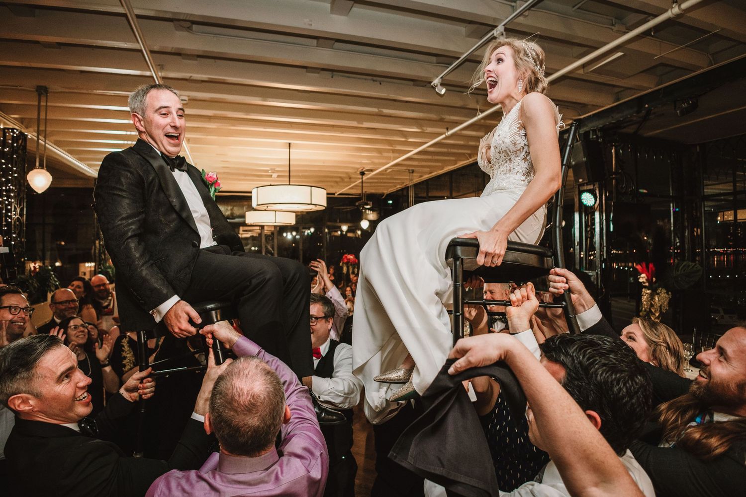 Couple being lifted on chairs during traditional wedding celebration dance.