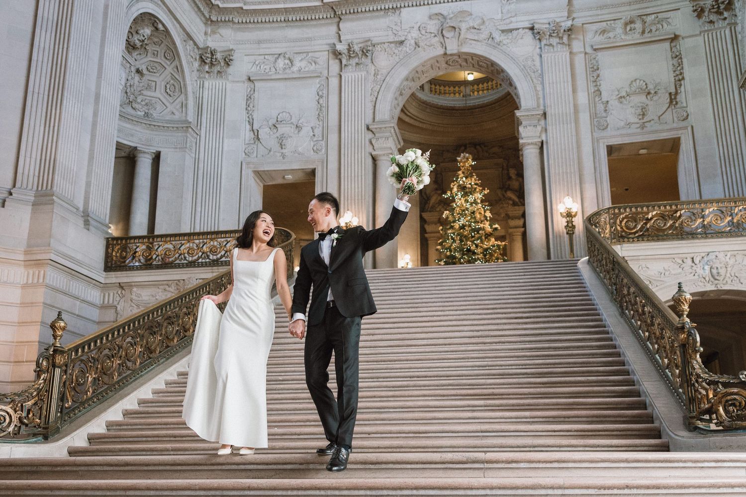 Celebratory moment on grand marble staircase with Christmas tree in background.