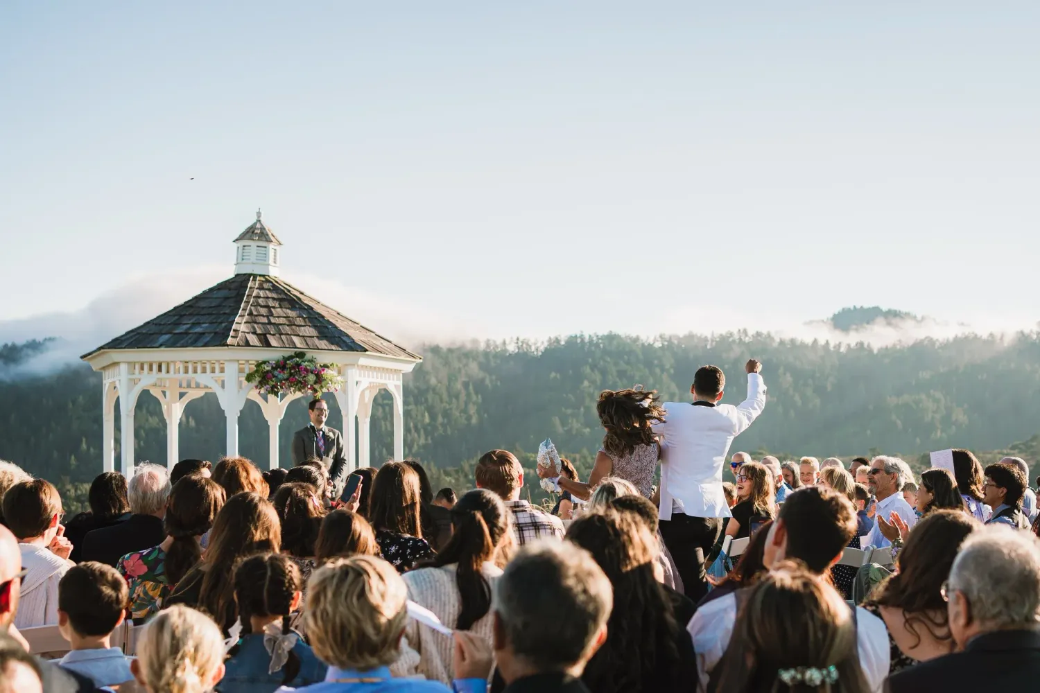 A large crowd gathers around a white gazebo on a hilltop during an outdoor celebration or ceremony.