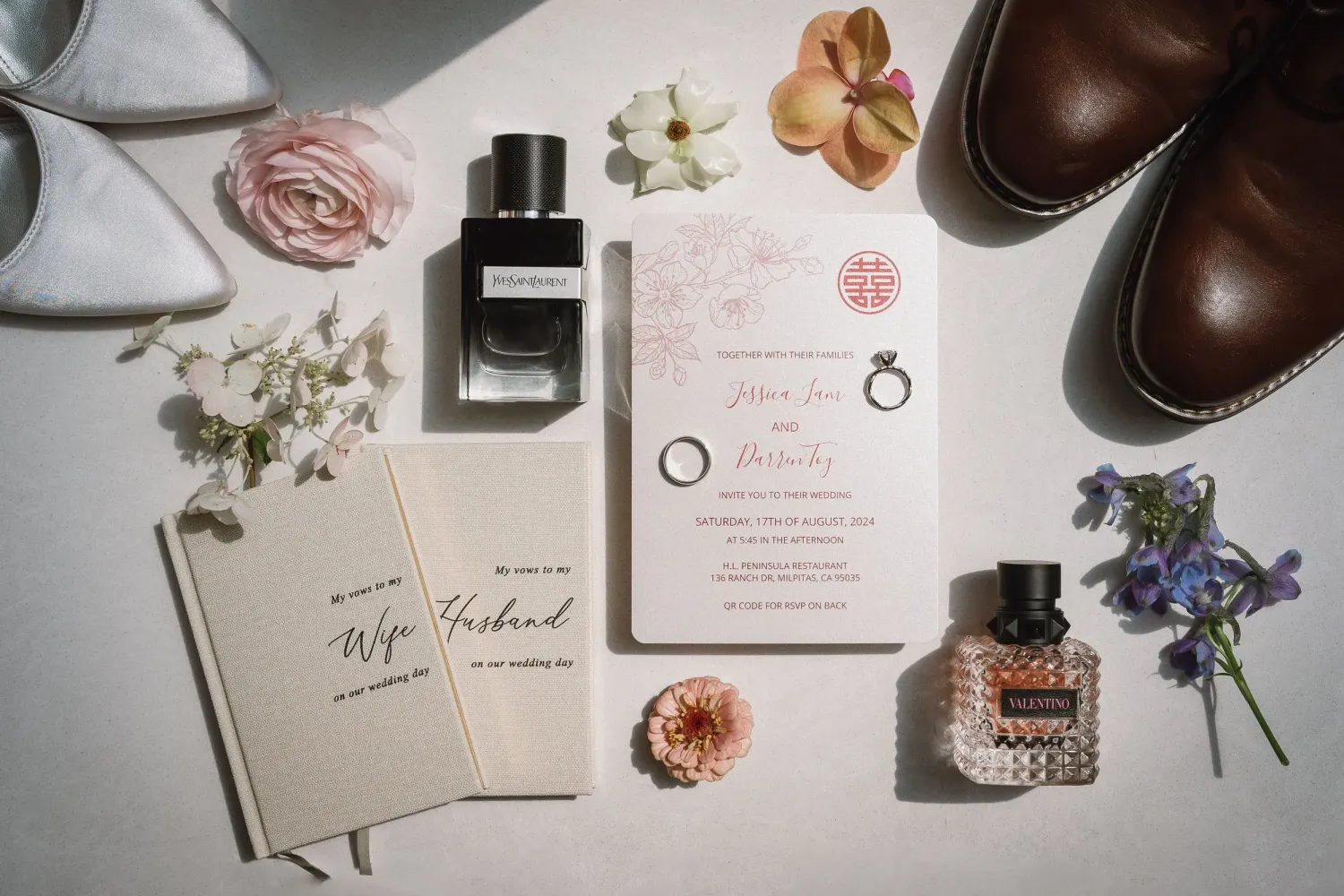Wedding invitation suite with floral details, rings, and accessories arranged on white background.