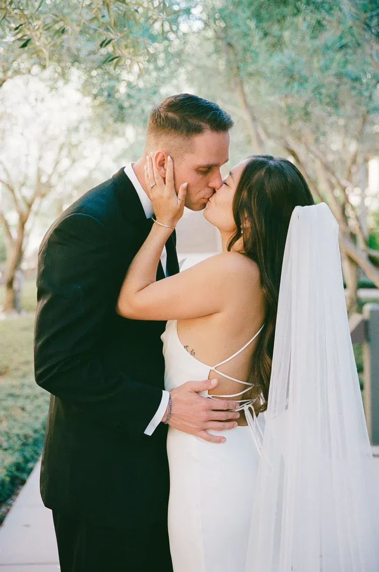Romantic wedding couple embracing in a garden setting with flowing white veil.