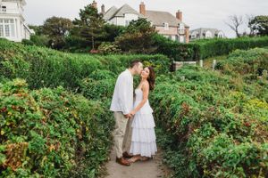 A romantic moment shared in a lush garden path with coastal houses visible in the background. Cliff Walk, Newport, RI