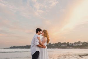 A romantic sunset moment between two people on a beach with warm glowing sky. First beach Newport, RI RI engagement photographer,