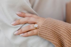 Close-up of hands showing off an engagement ring against cream and tan sweaters. Engagement Session Newport, RI