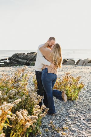 A romantic moment captured on a rocky beach with wildflowers in the foreground. Engagement Session Newport, RI