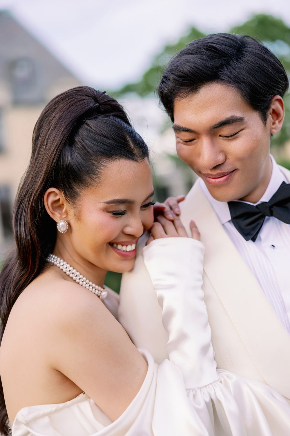 A joyful bride and groom share an intimate moment together, with the bride wearing pearls and an off-shoulder gown.