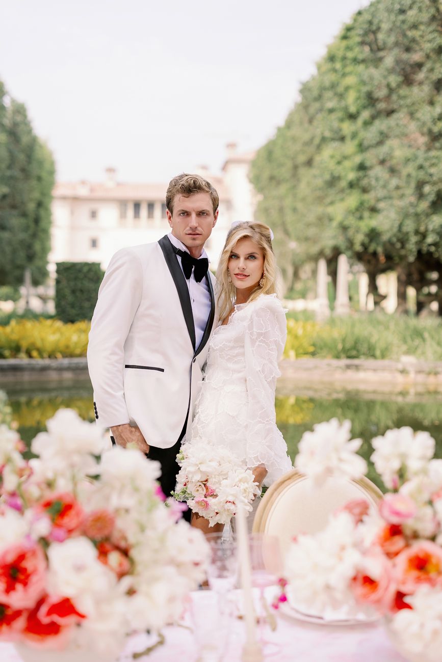 Wedding portrait of couple in white tuxedo and lace dress by garden pool.