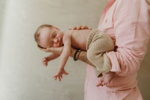 A sleeping newborn wearing knit clothing being gently cradled.