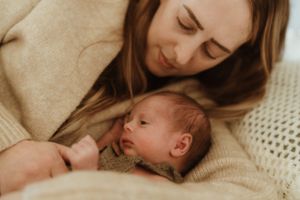 Sweet candid moments of parents cuddling with their newborn on a beige blanket.