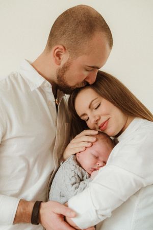 Intimate family portrait with newborn baby in white minimalist setting.