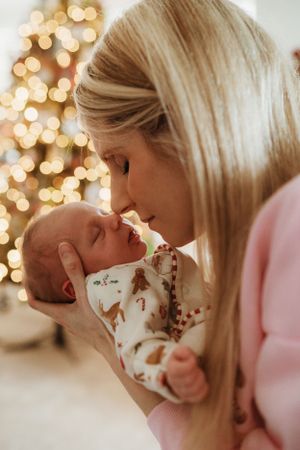 A tender moment between parent and baby with Christmas tree lights creating a warm glow.