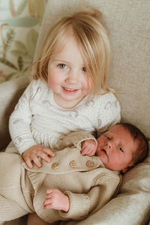 Lifestyle newborn session with siblings on neutral linen background.