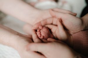 Close-up photo of a newborn baby's tiny feet being gently held by adult hands in soft lighting.