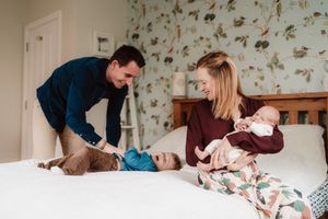 A family shares a joyful moment together on a bed with floral wallpaper in the background.