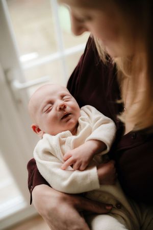 A tender moment shows a newborn baby wrapped in a white blanket being cradled in loving arms.