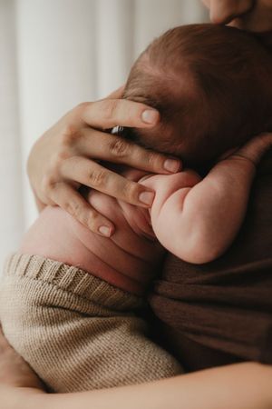 Gentle hands cradle a tiny baby wearing a knit sweater in soft, warm lighting.