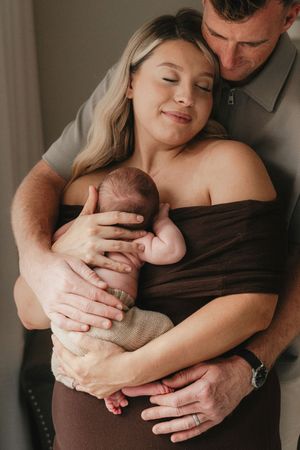 A tender family moment as parents embrace their newborn baby in soft natural lighting during an intimate photo session.