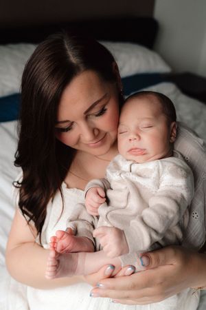 A tender sequence showing a mother cradling and bonding with a sleeping baby in white clothing on white bedding.