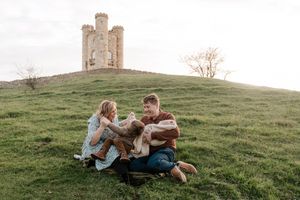 A couple embraces on a grassy hillside during a romantic outdoor photoshoot at sunset.
