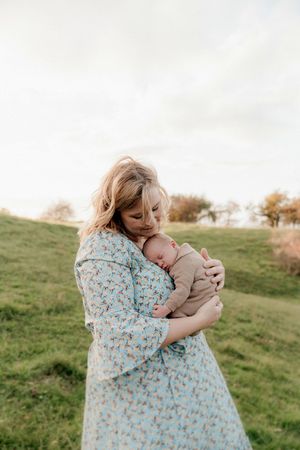 A series of outdoor photos showing gentle embraces between siblings on a grassy hillside in soft natural lighting.