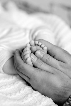 Close-up black and white photo of hands tenderly holding a newborn baby's tiny feet against white fabric.
