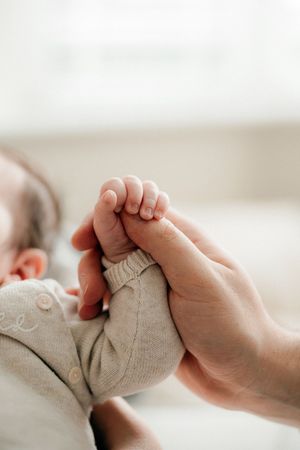 A tiny baby foot being gently held by an adult hand against a soft beige knit fabric background.