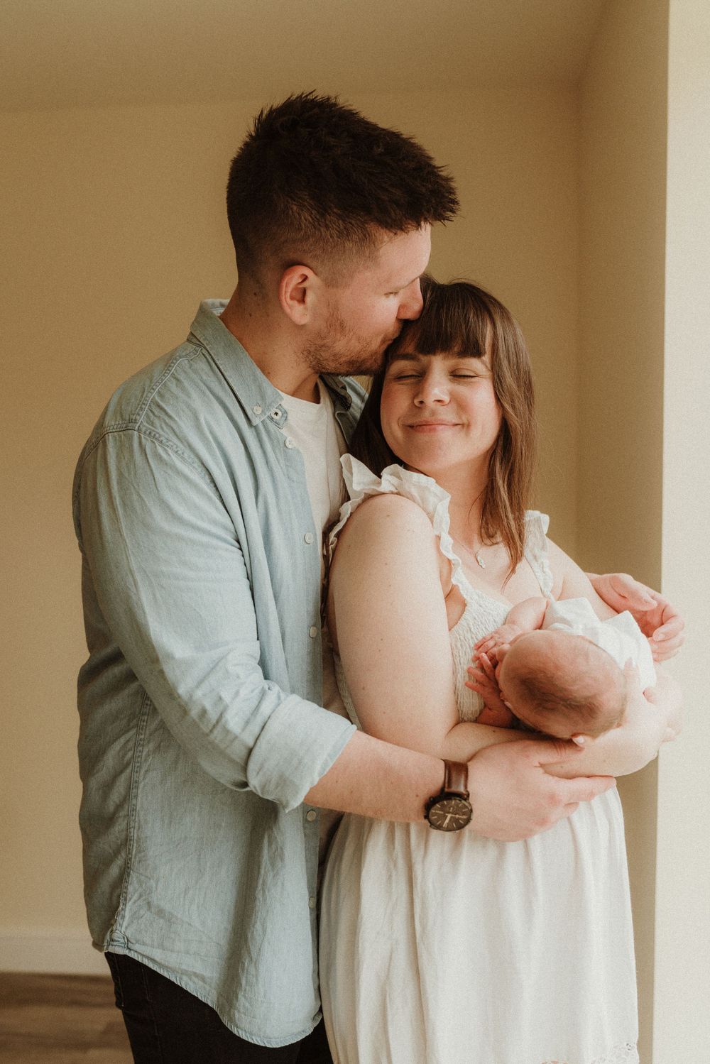 Intimate indoor family portrait series showing parents bonding with their newborn.