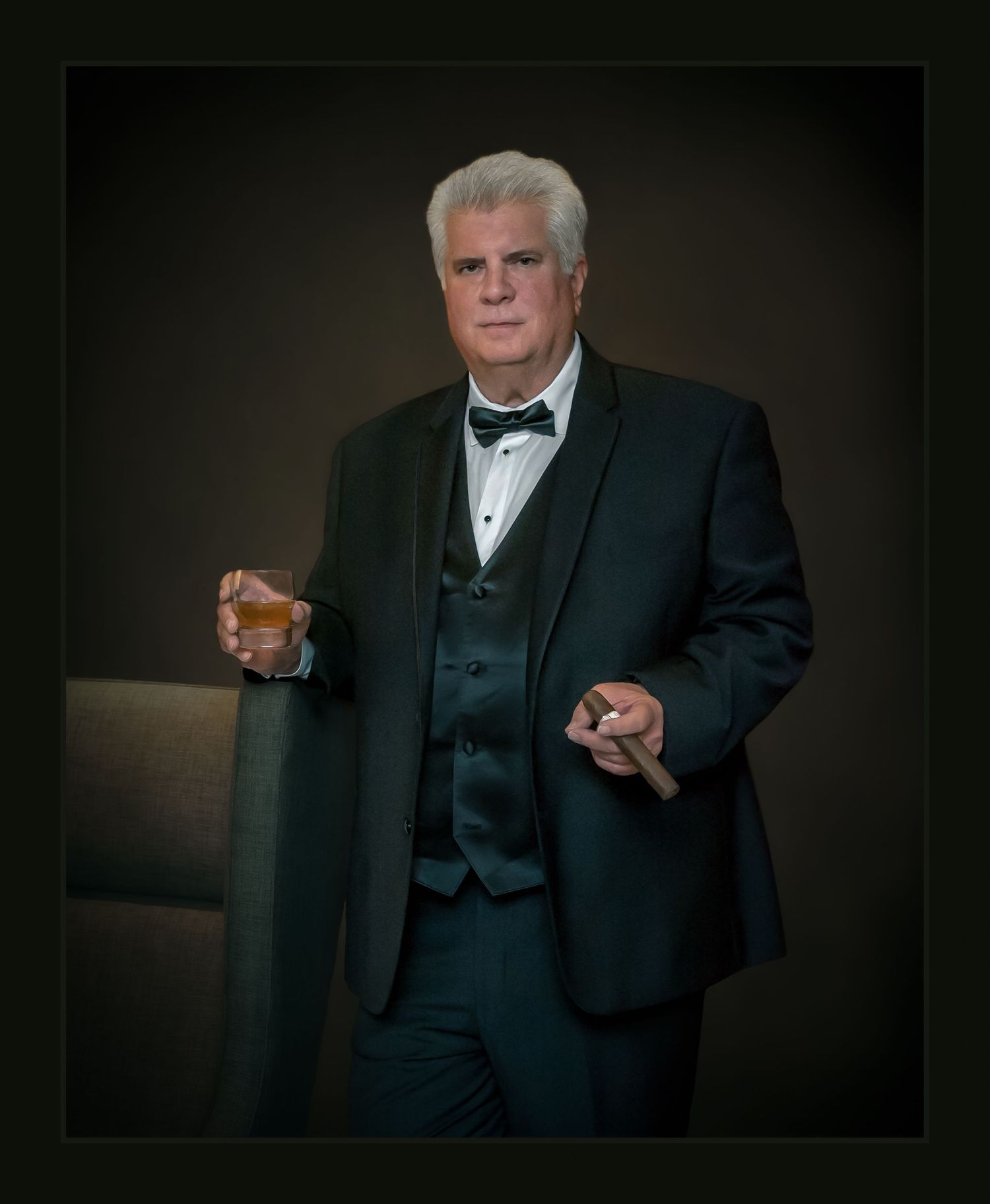 Elegant older man in black tuxedo holding whiskey glass & cigar, posing confidently in a formal portrait. Best photographer Williamsburg VA